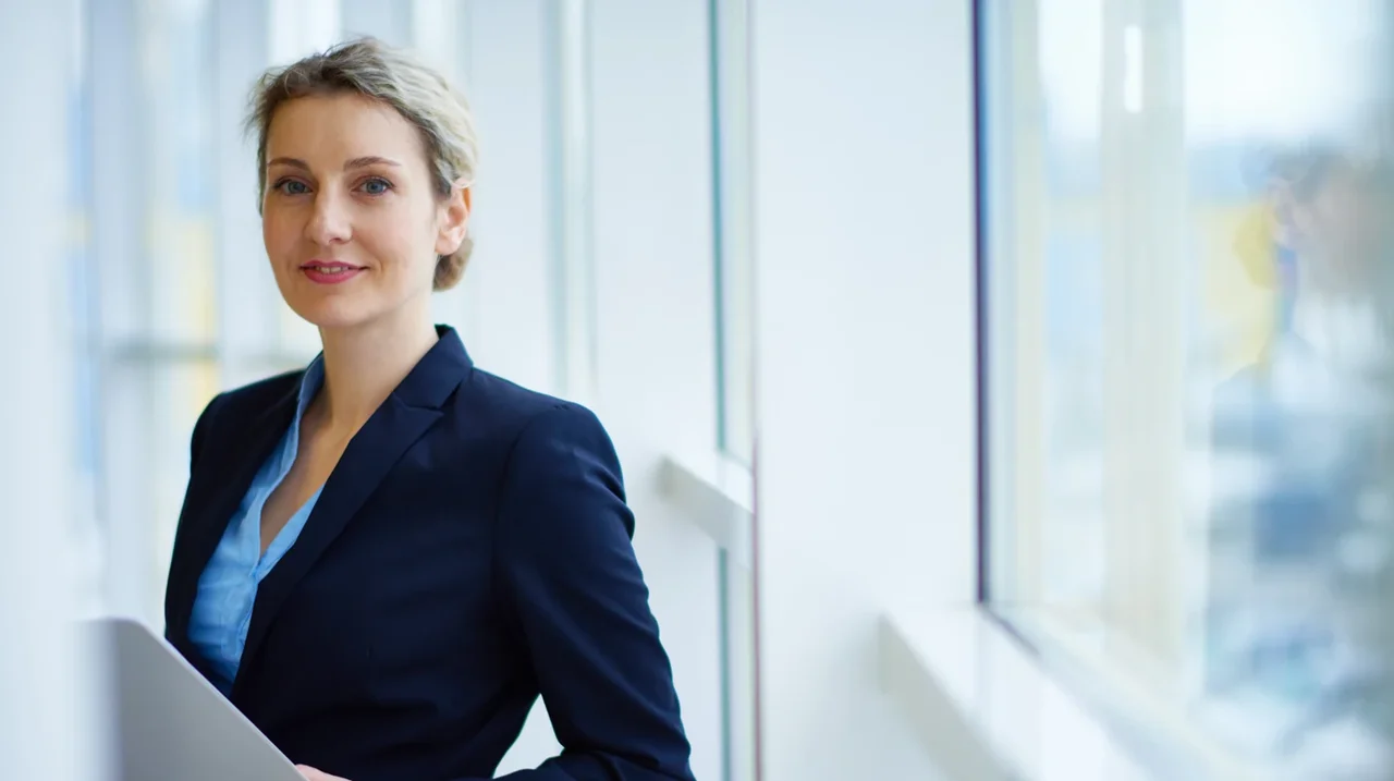 Professional in a blue jacket standing in a bright workplace.