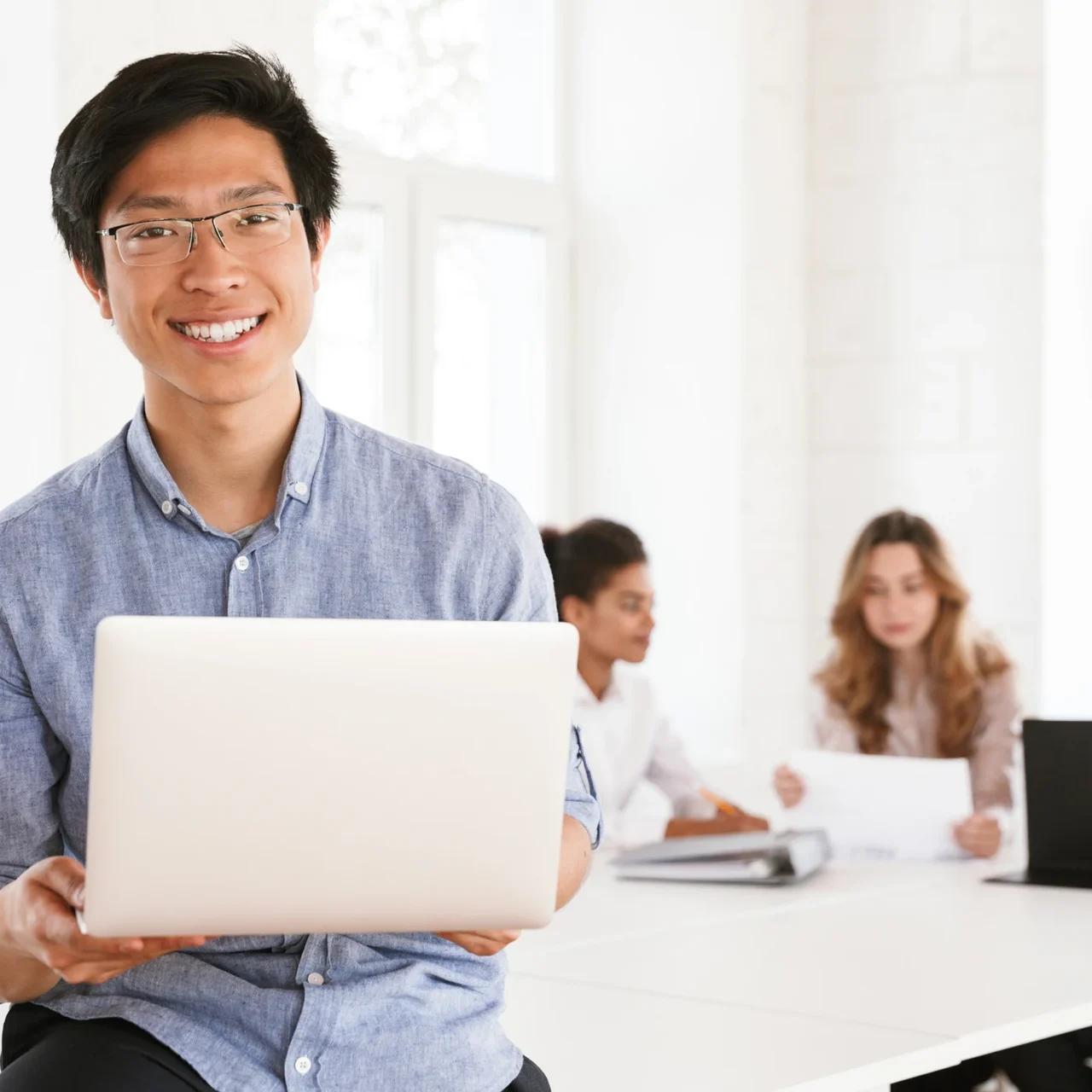Professional holding a laptop in a shared workspace.