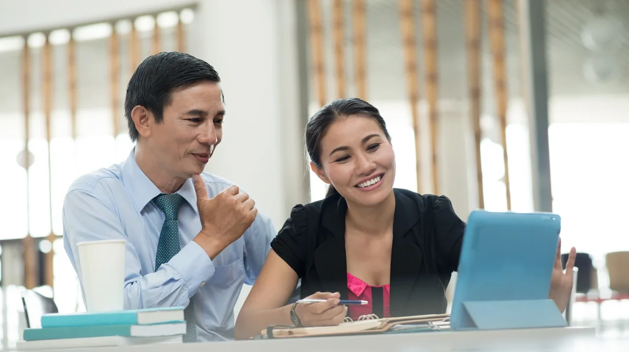 Two colleagues smiling while reviewing a laptop.