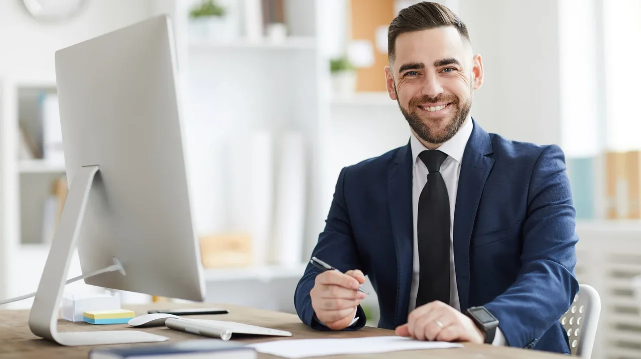 Professional smiling at a desktop computer.