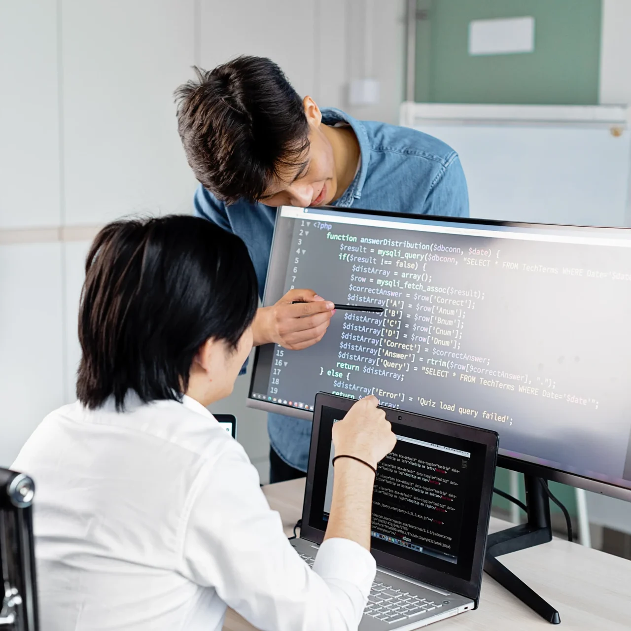 Colleagues discussing code at a desktop computer.