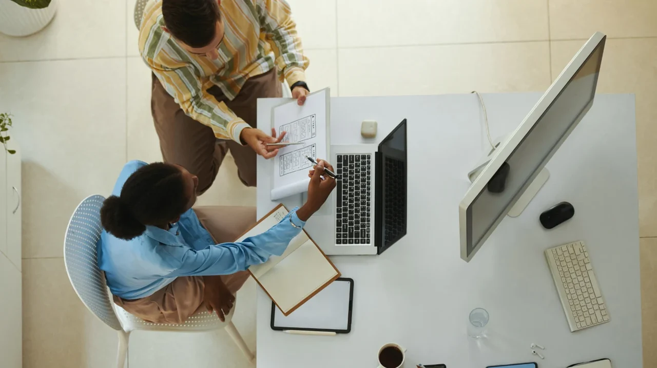 Overhead view of colleagues taking notes beside a laptop.