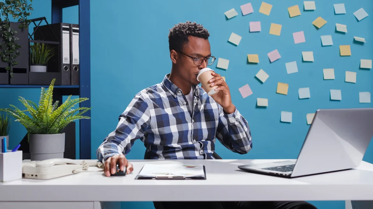 Professional making notes at a laptop beside a blue planning wall.
