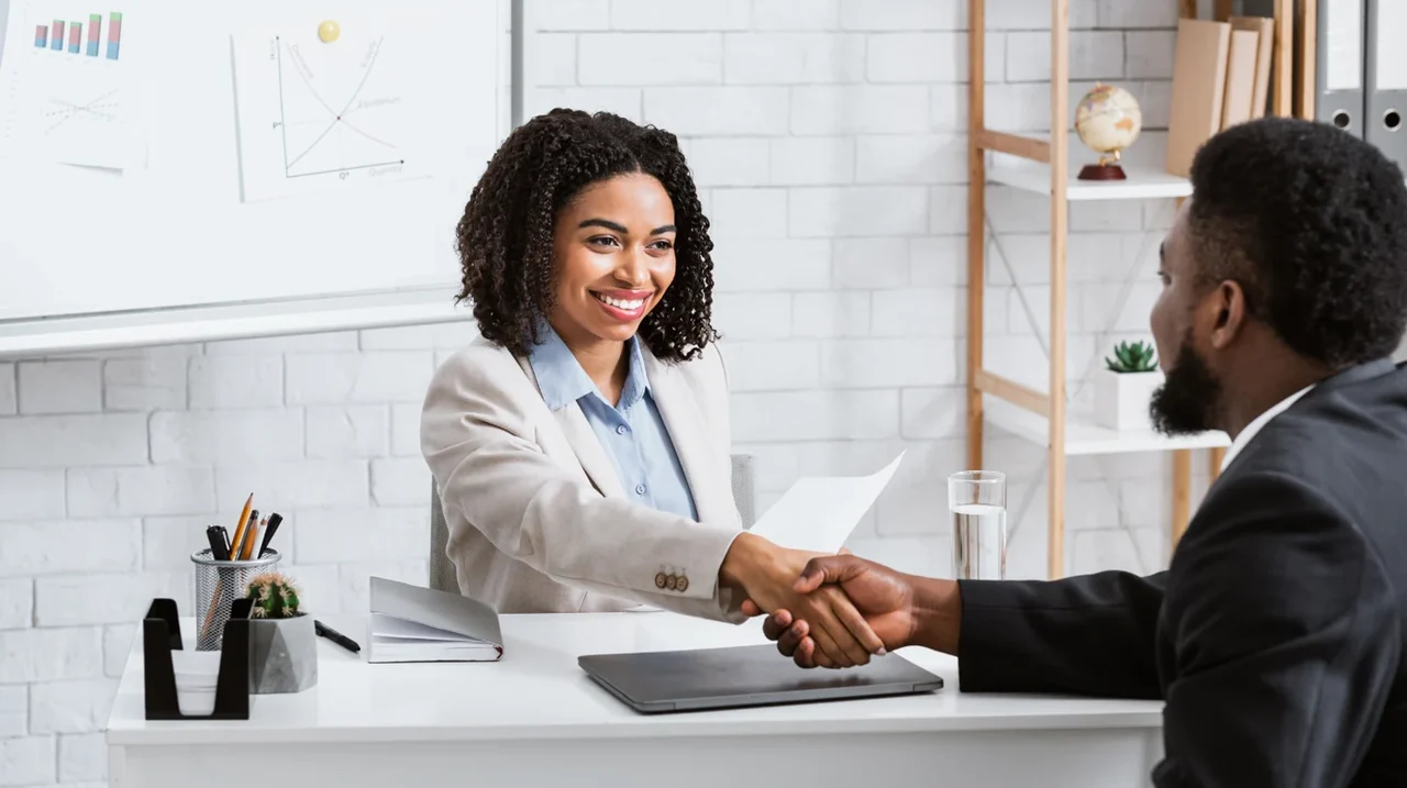Two professionals shaking hands across a desk.