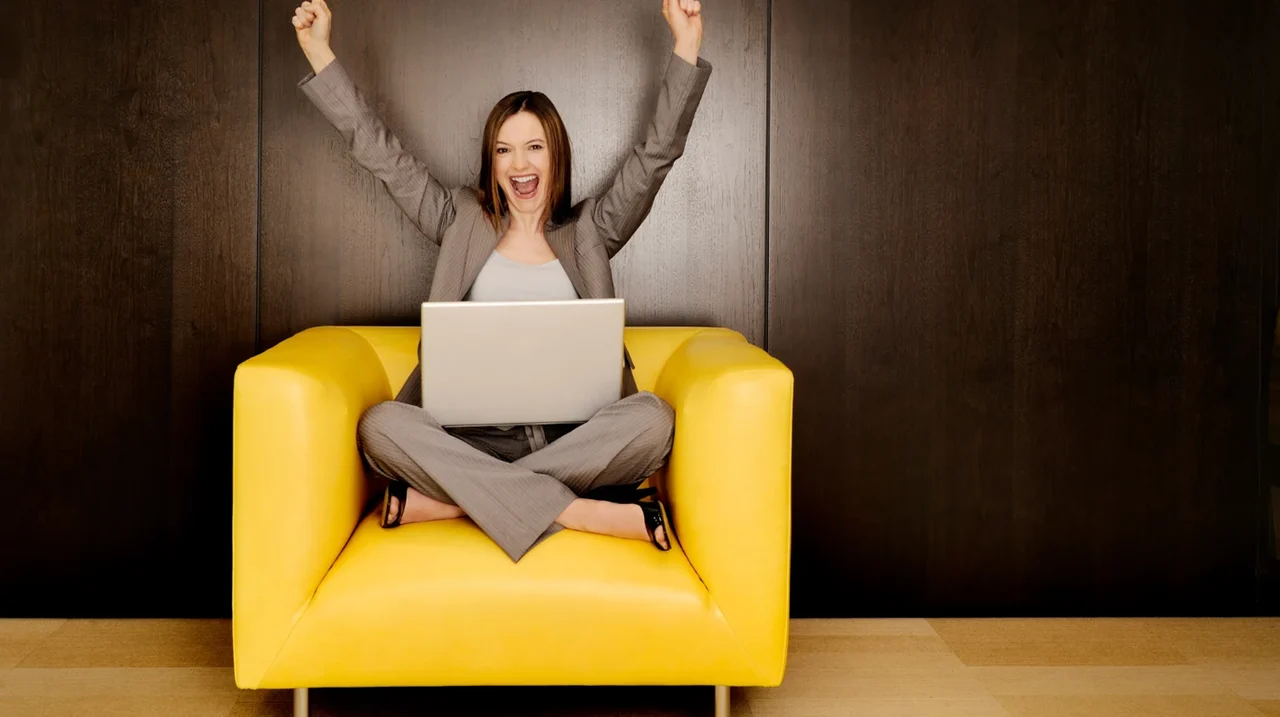 Professional celebrating with a laptop in a yellow chair.